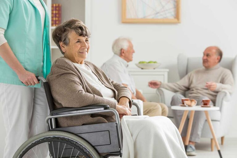 Family members and elderly residents sharing conversation and refreshments in a bright community room during a group event.