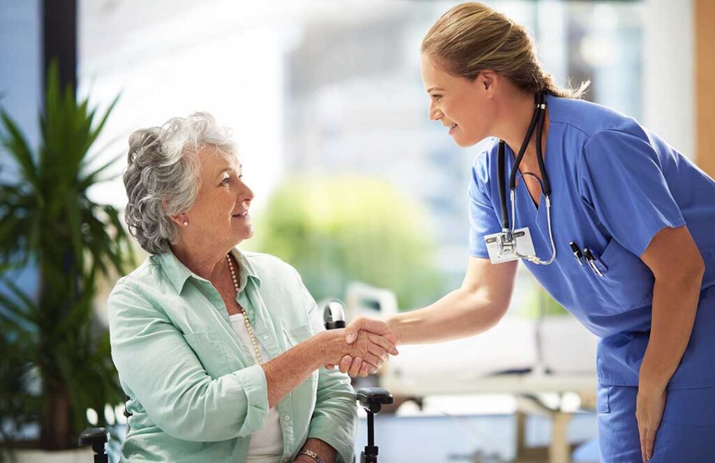 Older adult talking with a caregiver in a bright assisted living common room.
